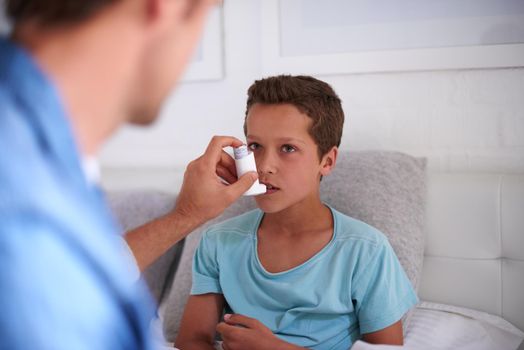 Take a deep breath in. a caring father giving his son an asthma pump at home.