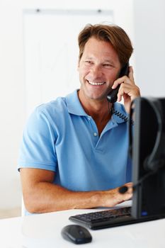 Thank you and have a great day. a smiling man using a telephone at his work desk.