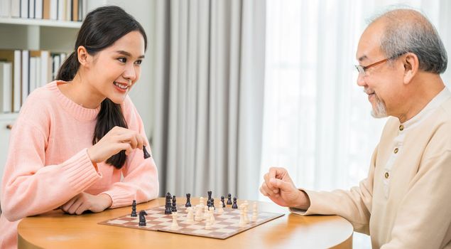 Beautiful young smile woman having fun sitting playing chess game with senior elderly at home