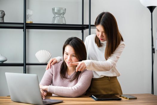 Asian mother and teenage daughter looking at laptop computer at home office