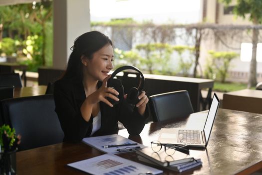 Attractive businesswoman holding headphone and watching webinar on laptop computer.