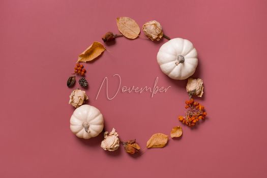 November inscription in wreath of pumpkin, leaves and flowers with berries top view