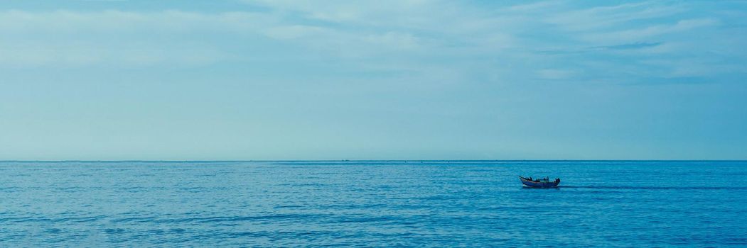 Simple background Calm dark blue sea fishing boat alone white pale Spindrift clouds Open way no limitations. BANNER LONG FORMAT