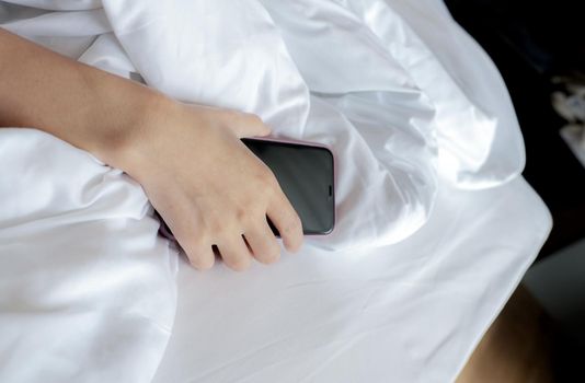 Woman sleeping in bed and hand holding mobile phone. Woman using smartphone in bedroom. Woman addicted using smartphone. Texting on cellphone with tired until falling asleep. Asleep with smartphone.