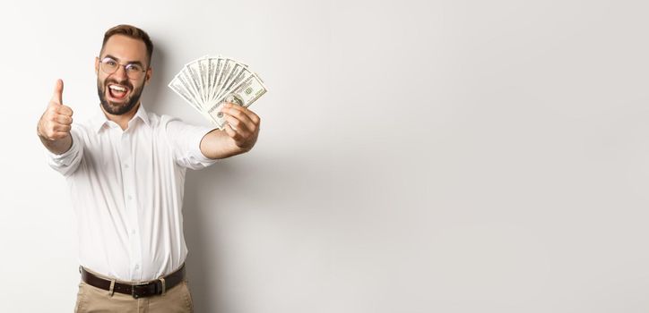 Excited man showing thumbs up and money, earning cash, standing over white background