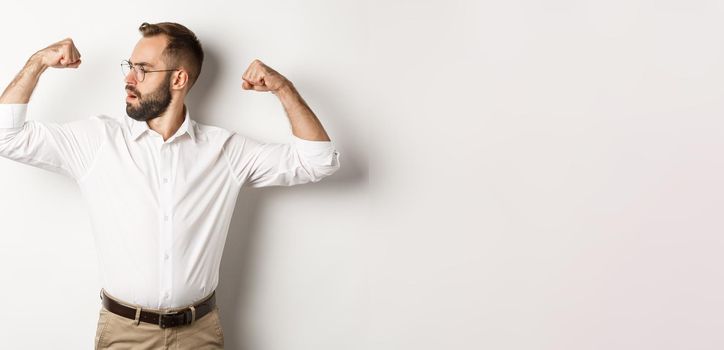 Successful businessman flex biceps, showing muscles and looking confident, feeling strong, standing over white background