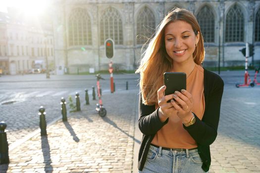 Attractive woman walking using mobile phone on urban background at sunset