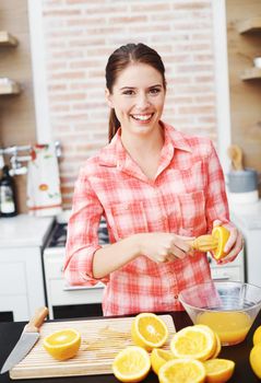 She enjoys staying healthy. An attractive young woman making fresh orange juice in her kitchen.