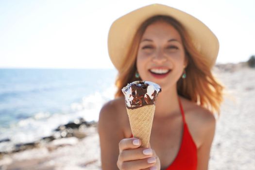 Close-up of beautiful bikini woman with hat offers an ice cream cone to the camera on the beach on summer. Focus on ice cream.