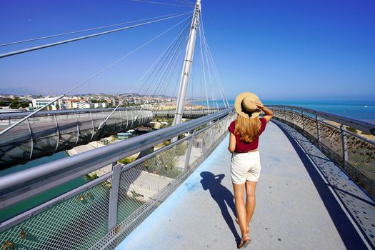 Young woman walking on Pescara modern bridge enjoying seascape from promenade in Abruzzo region, Italy