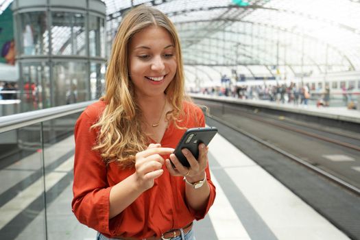 Smiling attractive Brazilian traveler passenger buys ticket online with smartphone in train station. Copy space.
