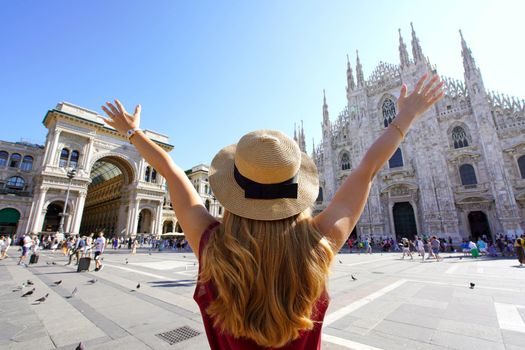 Excited young woman with arms raised in Milan Cathedral Square, Italy