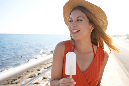 Beautiful girl with hat holding a white popsicle on the beach looking to the side