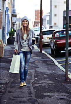 The urban life. Portrait of a beautiful young woman walking with a shopping bag and takeaway coffee in the city.