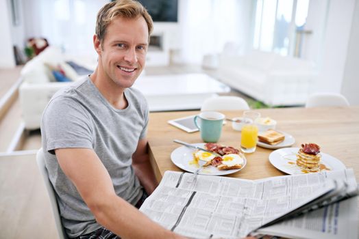 Enjoying his weekend pleasures. Portrait of a handsome man eating breakfast while reading the morning paper.
