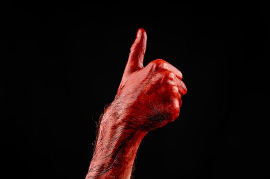 Male hand stained with blood on a black background holds the thumb up.