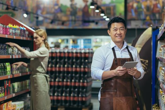 Portrait of a successful and happy Asian seller in a supermarket, a man in an apron