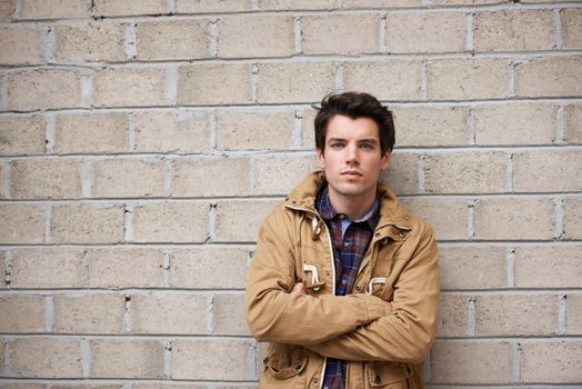 a young man leaning against a brick wall with his arms crossed