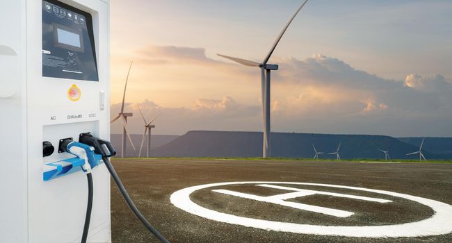 Electric vehicle charging station with asphalt helipad and wind turbines farm. Platform for helicopters. Sustainable and renewable energy. Green power. Sustainable development. Sustainable resources.