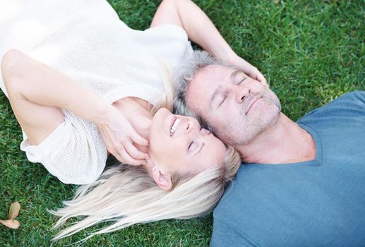 This is bliss. A mature couple lying on the grass smiling with eyes closed.