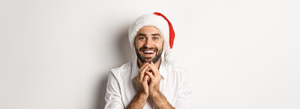 Party, winter holidays and celebration concept. Excited and hopeful man in santa hat looking at christmas gift with amazement, white background