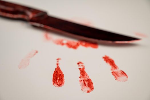 Bloody knife and hand prints in blood on a white table.