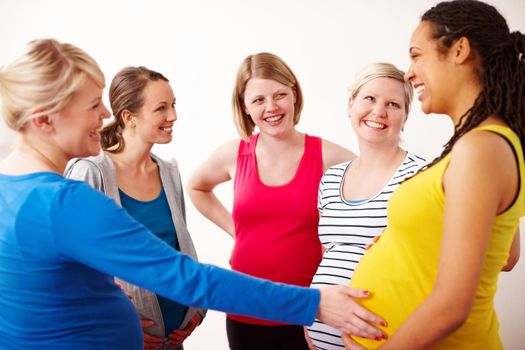 Hes a kicker. A young woman touching her pregnant friends belly while they stand in a group having a friendly discussion.
