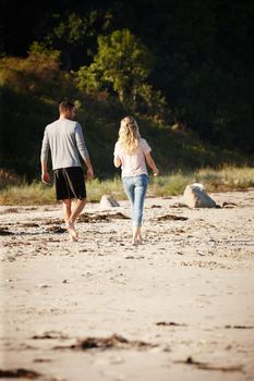 Spending a perfect time together. Rearview shot of a young couple walking along a sandy beach.