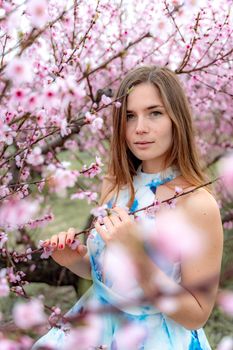 Young beautiful woman in blue dress and long hair is enjoying with blossoming peach trees