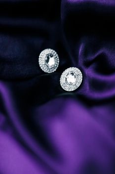 Luxury diamond earrings on dark violet silk fabric, holiday glamour jewelery present