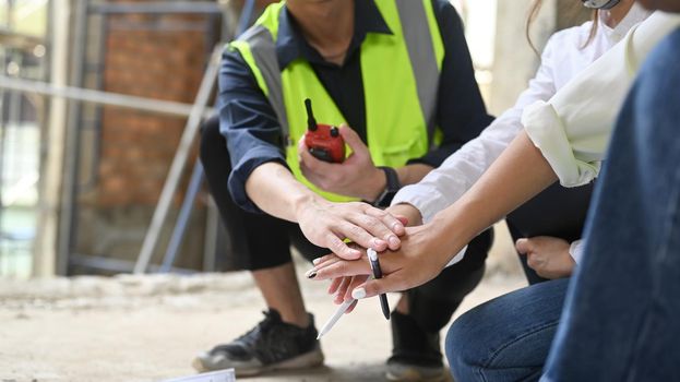 Cropped image of engineer and architects sitting in construction site floor and stacking hands together