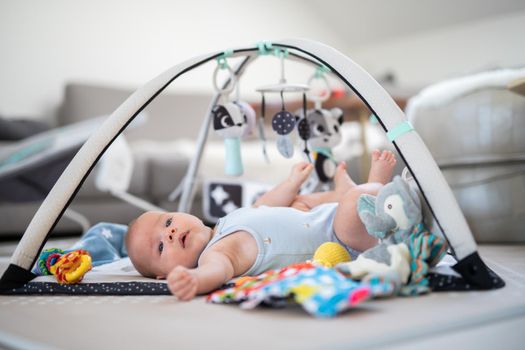 Cute baby boy playing with hanging toys arch on mat at home Baby activity and play center for early infant development. Baby playing at home