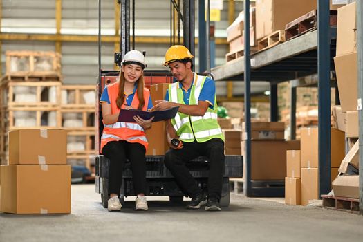 Warehouse workers, sitting on forklift truck and checking newly arrived goods in large warehouse