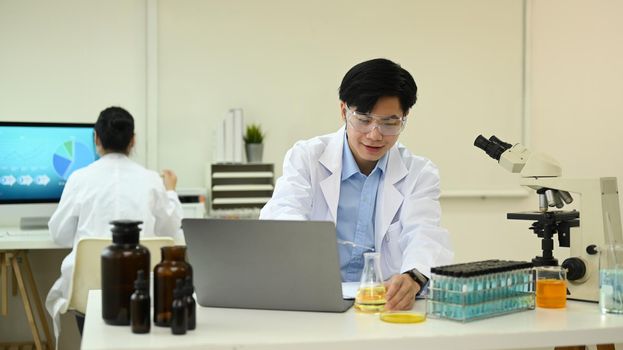 Asian man scientist in white lab coat using laptop and summarising information for scientific report