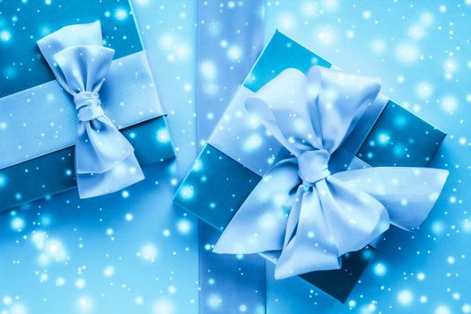 Winter holiday gifts and glowing snow on frozen blue background, Christmas presents surprise