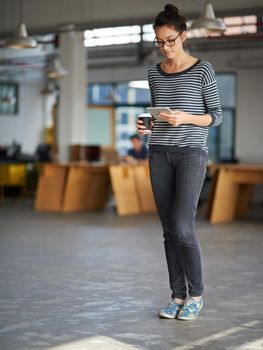 Tech keeping her in touch. Young woman holding a takaway coffe and looking at her digital tablet in an open plan office.