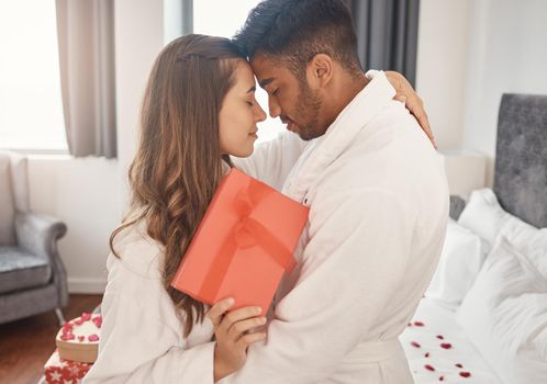 Interracial couple, love bond or hug on valentines day date or anniversary celebration in house bedroom, hotel or home interior. Romantic trust, security or safety for indian man and woman with gift