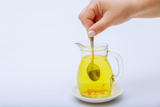 A woman stirs stamens in saffron tea in a transparent jug on a white background.