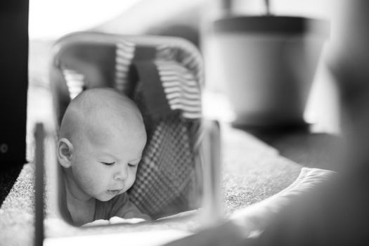 Beautiful shot of a cute baby boy looking at his reflection in the mirror. Black and white image.