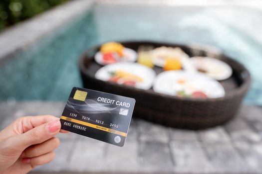 Hand holding credit card with floating breakfast in the pool on luxury villa, payment luxury travel.