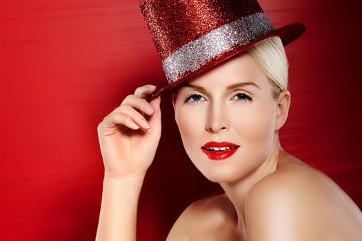 She was born for Hollywood. Portrait of a beautiful showgirl with red lipstick and a sparkly red hat against a red background.