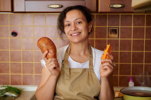 Beautiful Hispanic woman, a housewife holding a sweet potato and batata wedges and smiling a toothy smile at the camera