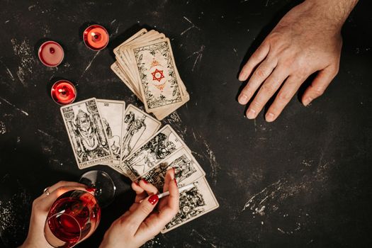 Tarot cards and female hands of fortune teller and client on black magic table