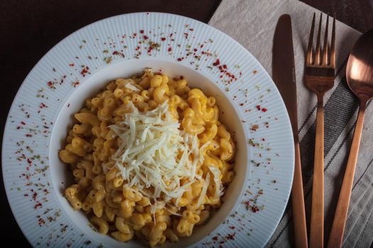 Mac and cheese, american style macaroni pasta with cheesy sauce on dark rustic table, top view