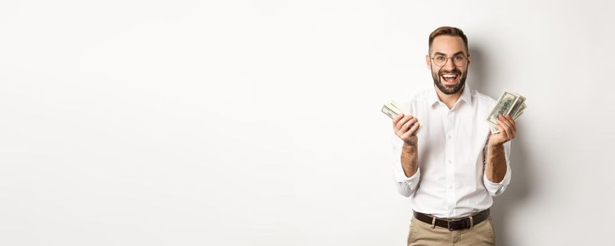 Handsome successful business man counting money, rejoicing and smiling, standing over white background