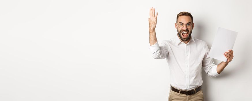 Angry businessman shouting and showing bad report, looking disappointed and frustrated, standing over white background