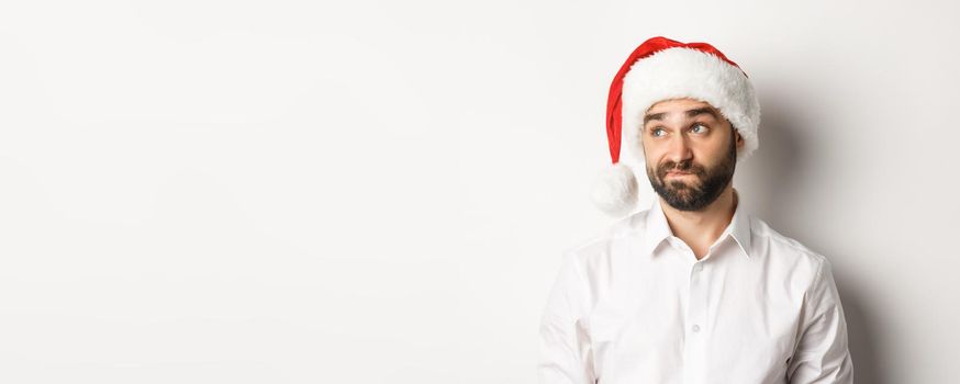 Close-up of skeptical guy in santa hat looking doubtful left, grimacing with hesitation, white background