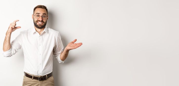 Businessman showing small gesture, looking displeased, shrugging confused, standing against white background