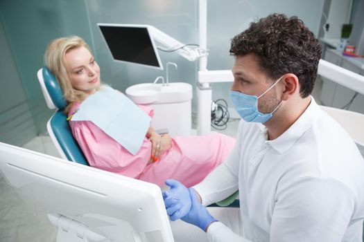 Experienced dentist working at his clinic, talking to mature patient