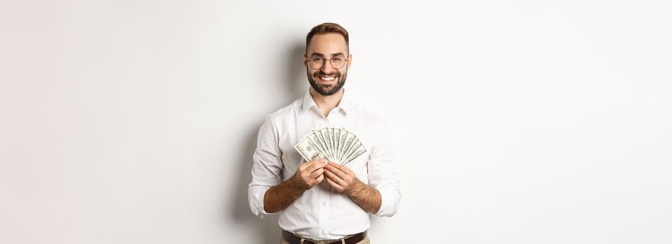 Smiling handsome man holding money, showing dollars, standing over white background